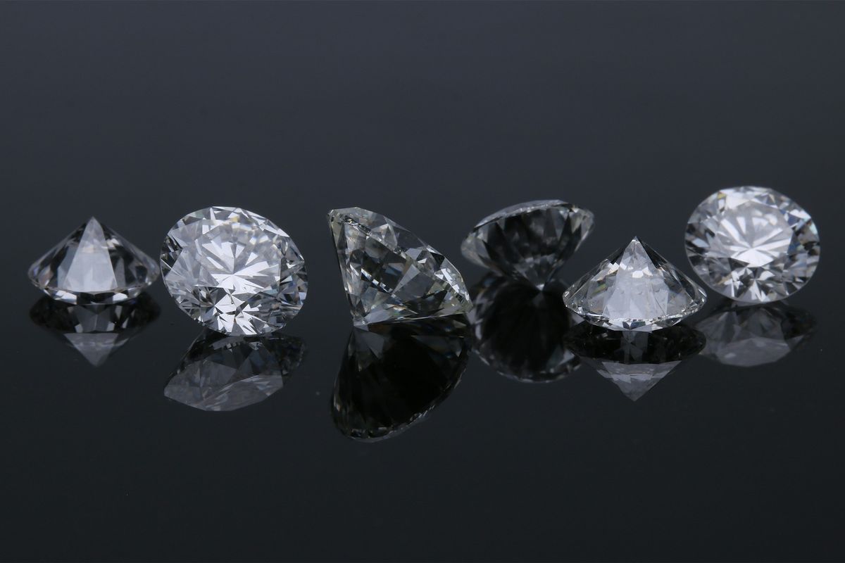 Six loose brilliant-cut diamonds in a row on a dark reflective surface
